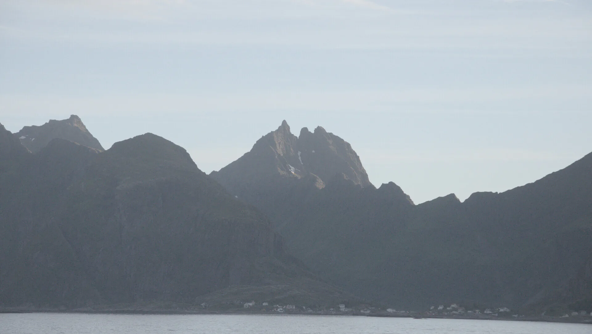 Dunkle, zackige Bergsilhouette über einem Fjord im Abenddunst